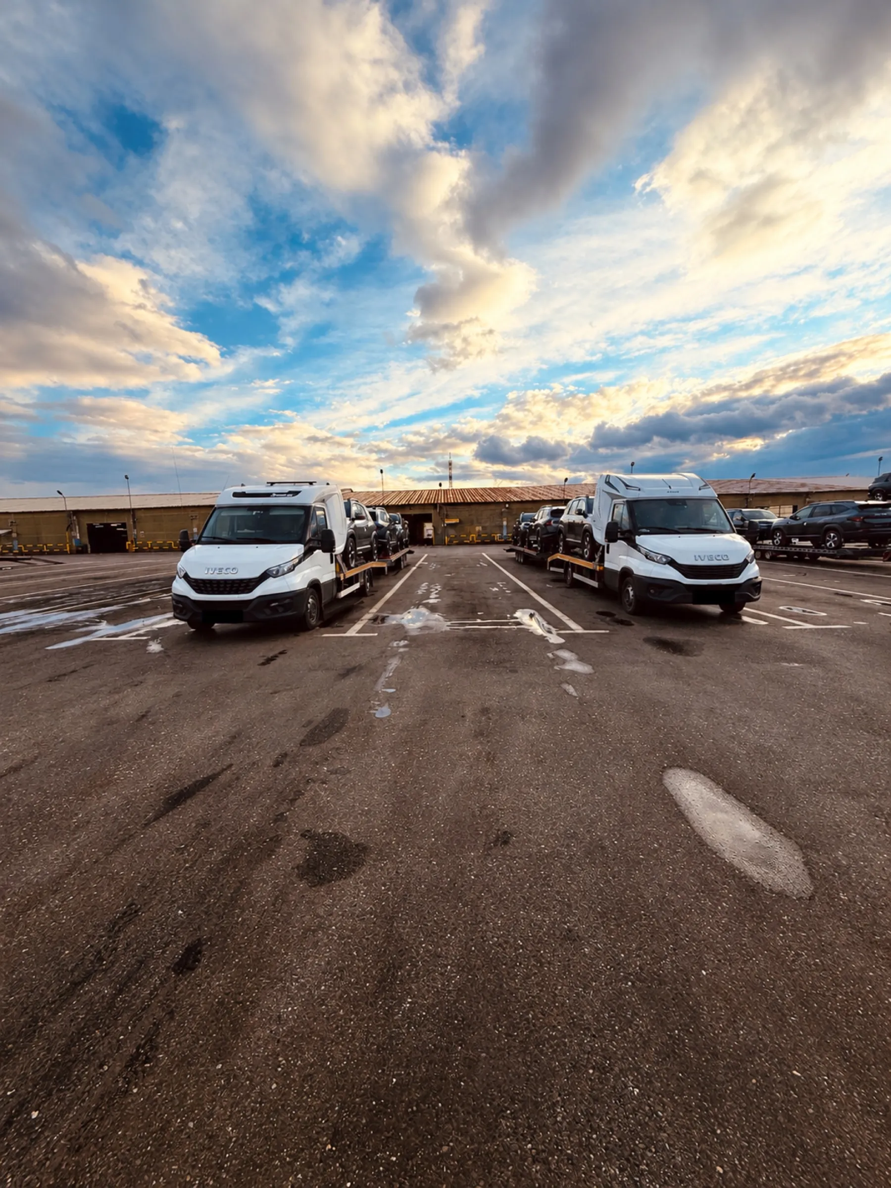 Autoplatformele Diava Cars încărcate, parcate una lângă alta la un centru logistic, cu cer dramatic