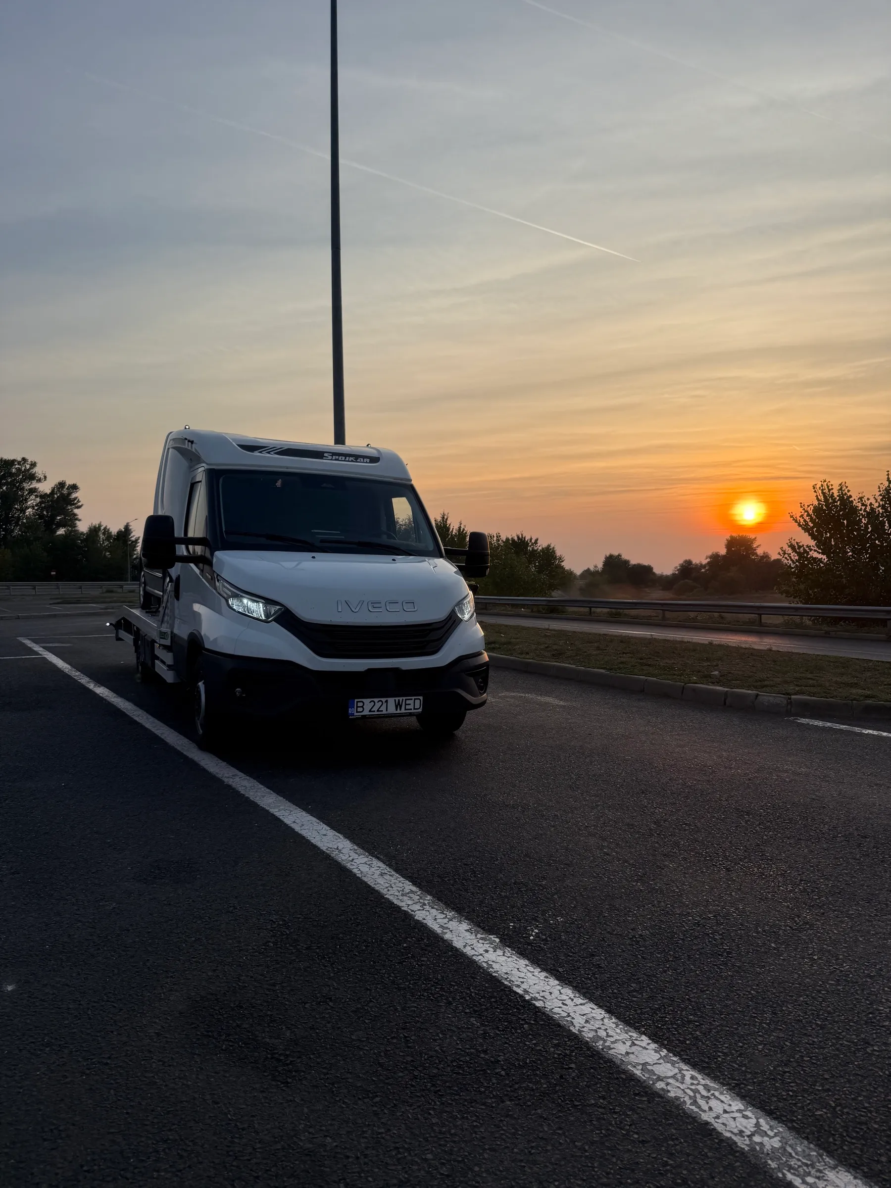Autoplatformă Diava Cars Iveco Daily oprită pe autostradă la apus, cu un autoturism încărcat