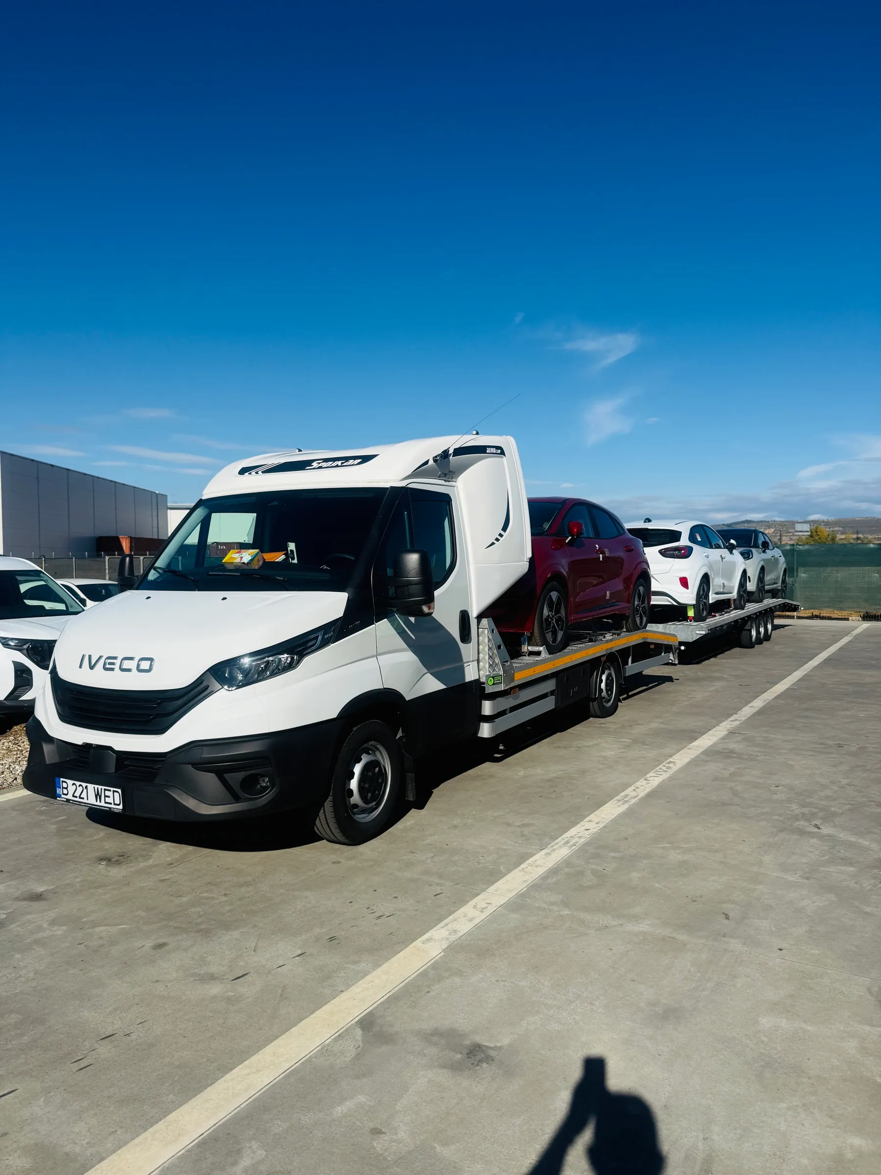 Autoplatforma Diava Cars cu remorcă, încărcată cu trei autoturisme, sub cer senin
